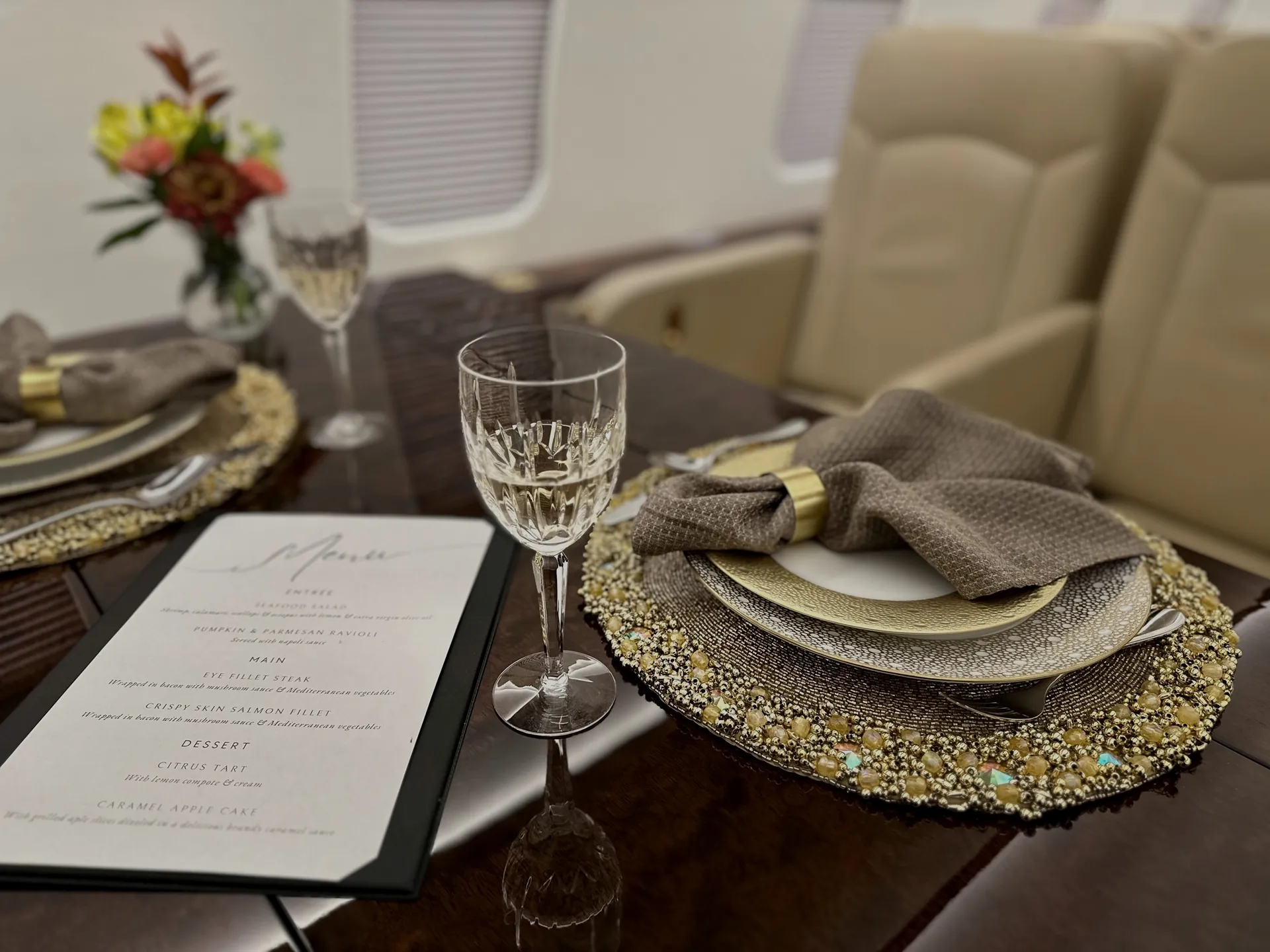 Fine-dining place setting with a gold charger plate and crystal glass inside a private jet cabin